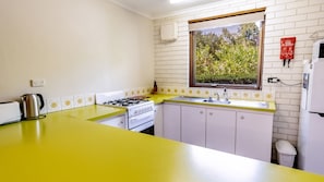 A compact kitchen with a yellow countertop, white cabinets, a gas stove, and a window with a view of greenery.