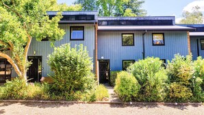 Un bâtiment moderne à deux étages, avec une façade bleue, une porte d’entrée et un petit porche.