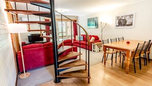 Un intérieur moderne avec un escalier en colimaçon, des canapés rouges, une table à manger avec des chaises et des œuvres d’art accrochées aux murs.