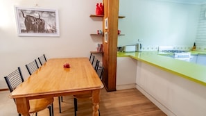 A dining area with a wooden table and chairs, a kitchen with a yellow countertop, and a framed picture on the wall.