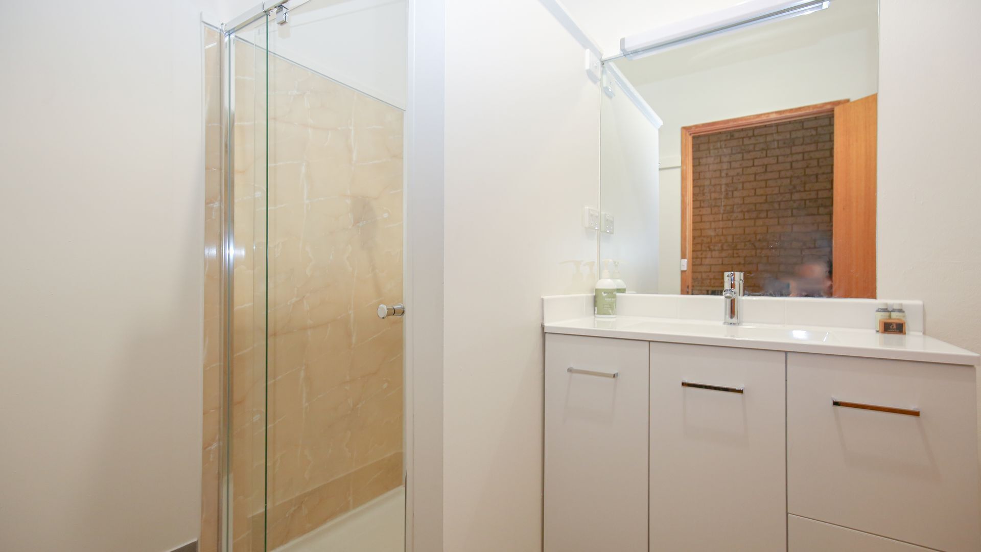 Une salle de bain moderne avec une douche à parois de verre, un meuble-lavabo blanc avec un miroir et un mur d’accent en briques.