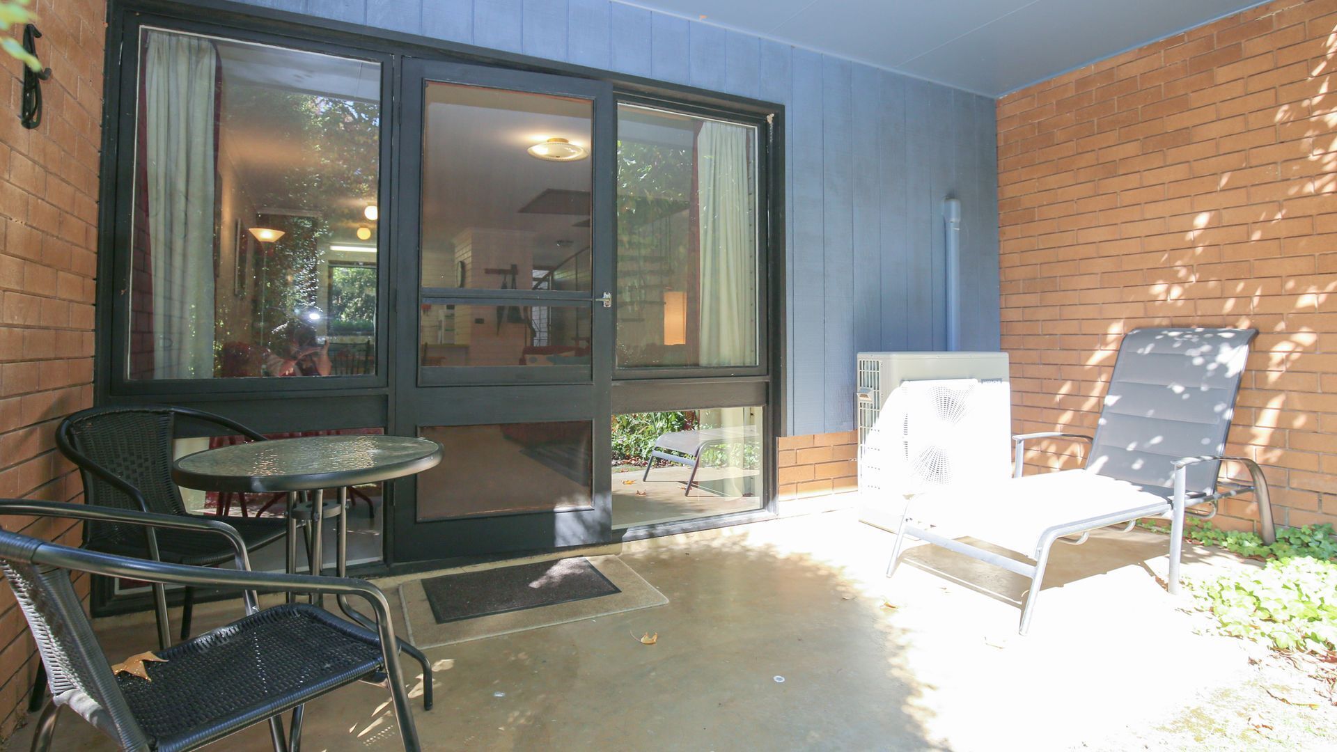 An outdoor patio with a table and chairs, a white fan, and a brick wall.