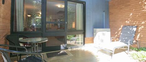 An outdoor patio with a table and chairs, a white fan, and a brick wall.