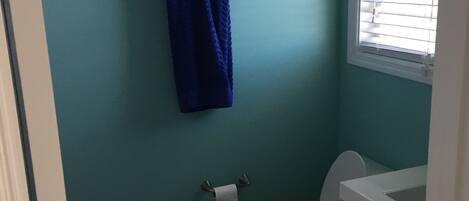 A bathroom with teal walls, a white toilet, a blue towel hanging on a rack, and a window with blinds.