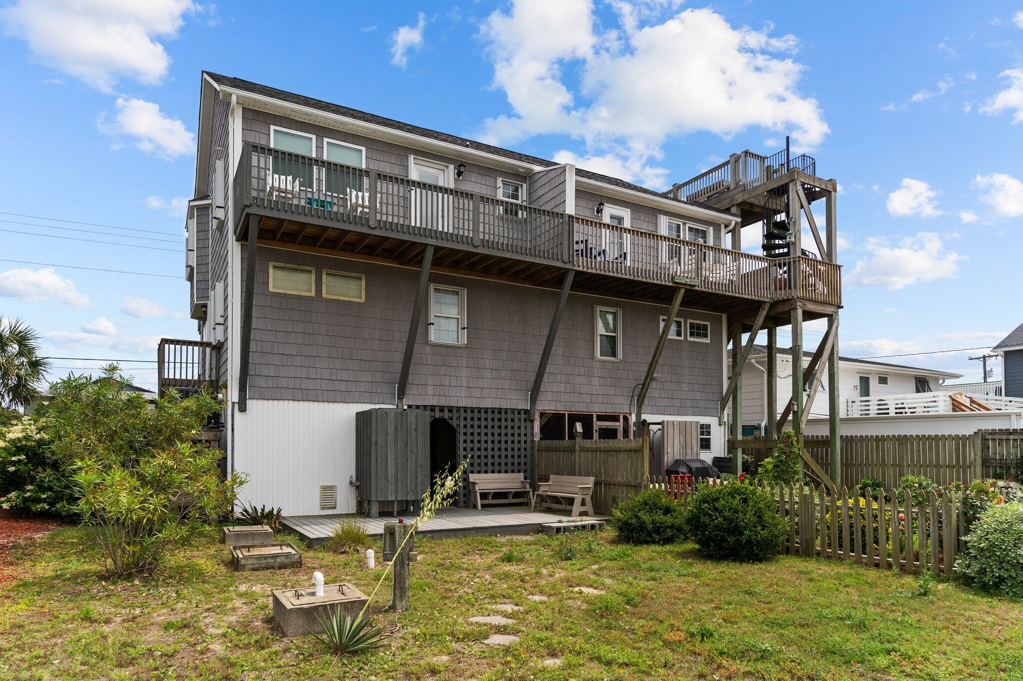 Une maison à deux étages avec un balcon à l’étage supérieur, une terrasse et une cour arrière clôturée.