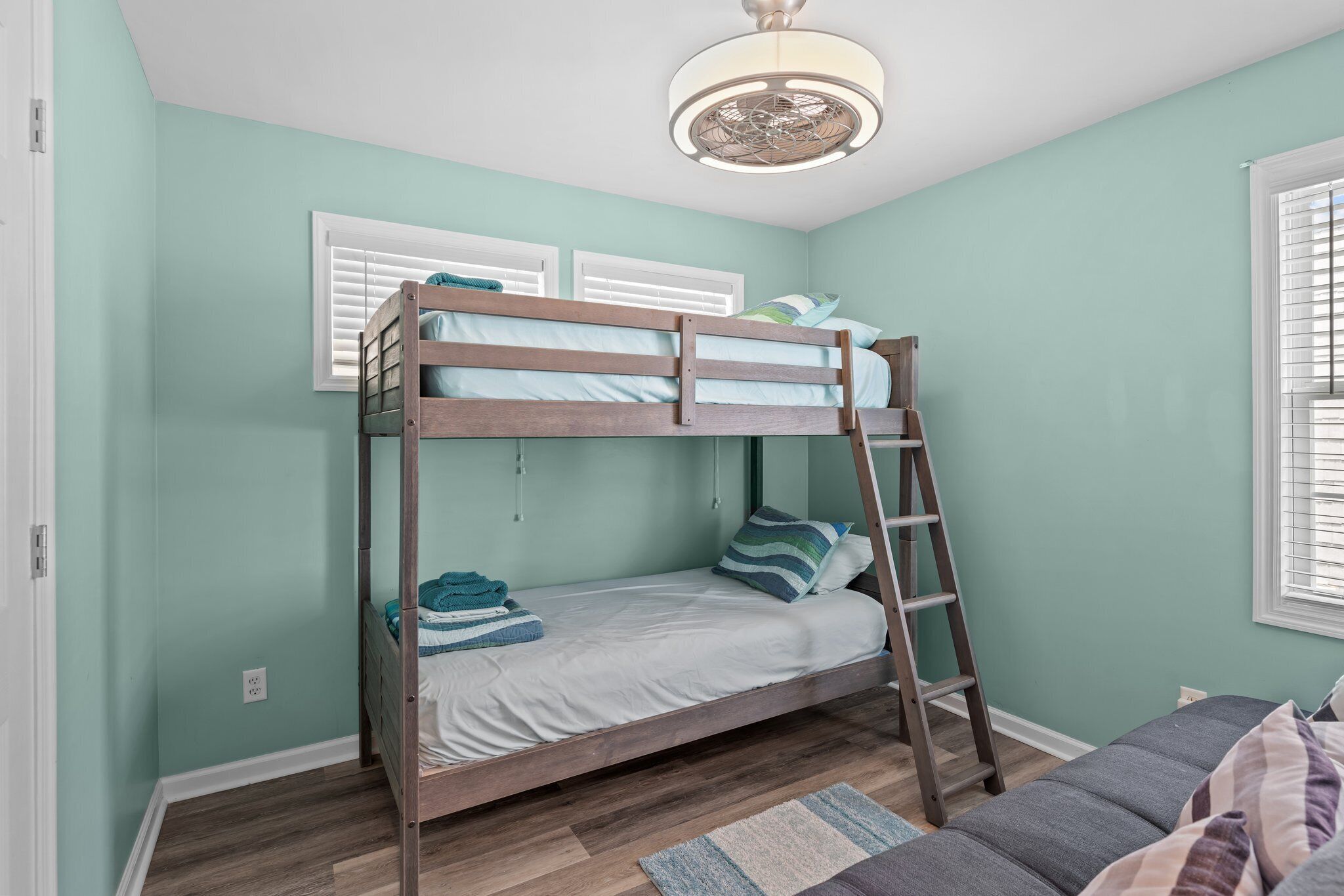 A bunk bed with a ladder, a window with blinds, and a ceiling fan.