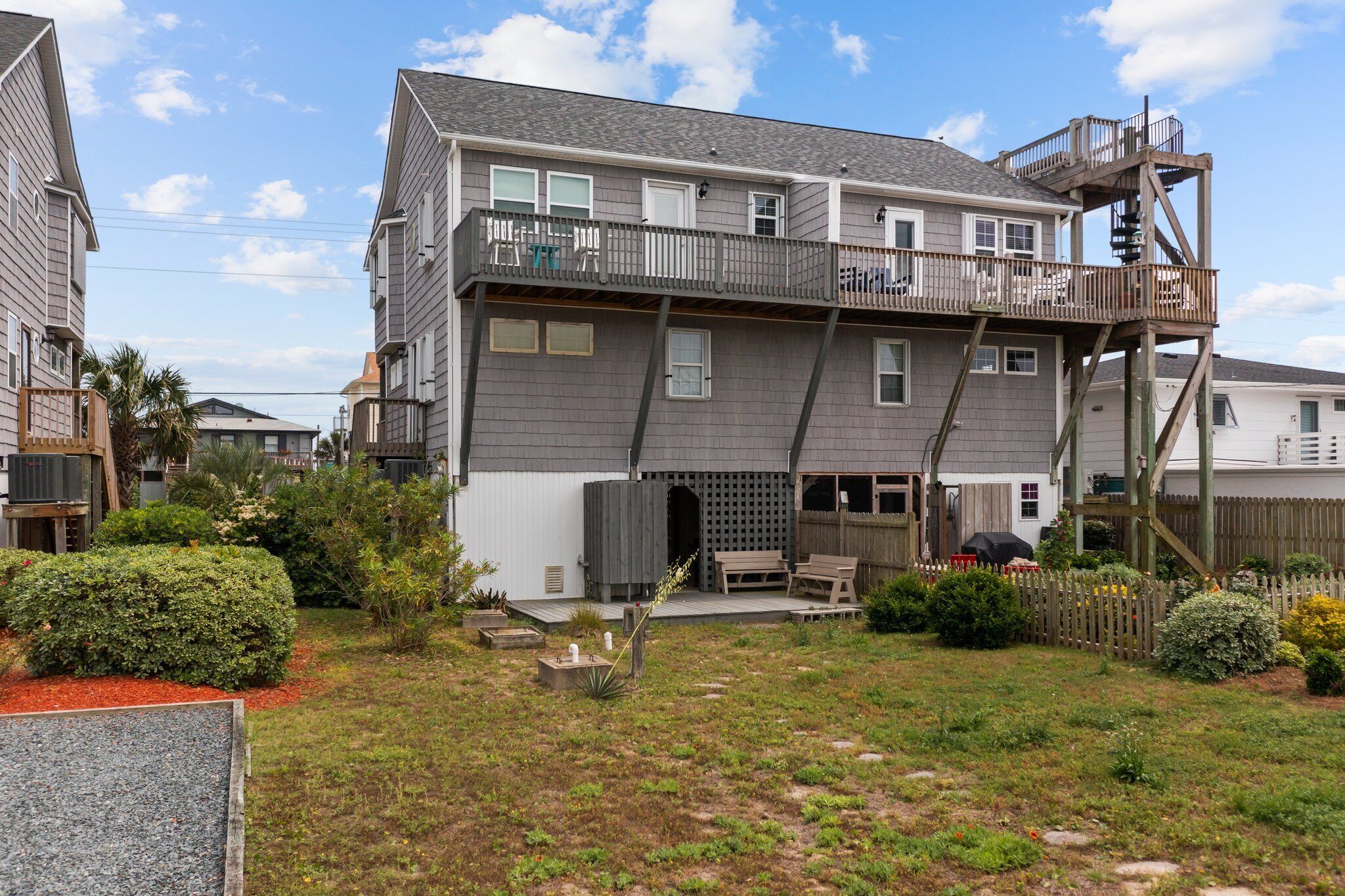 A two-story residential building with a balcony, a wooden deck, and a fenced backyard.