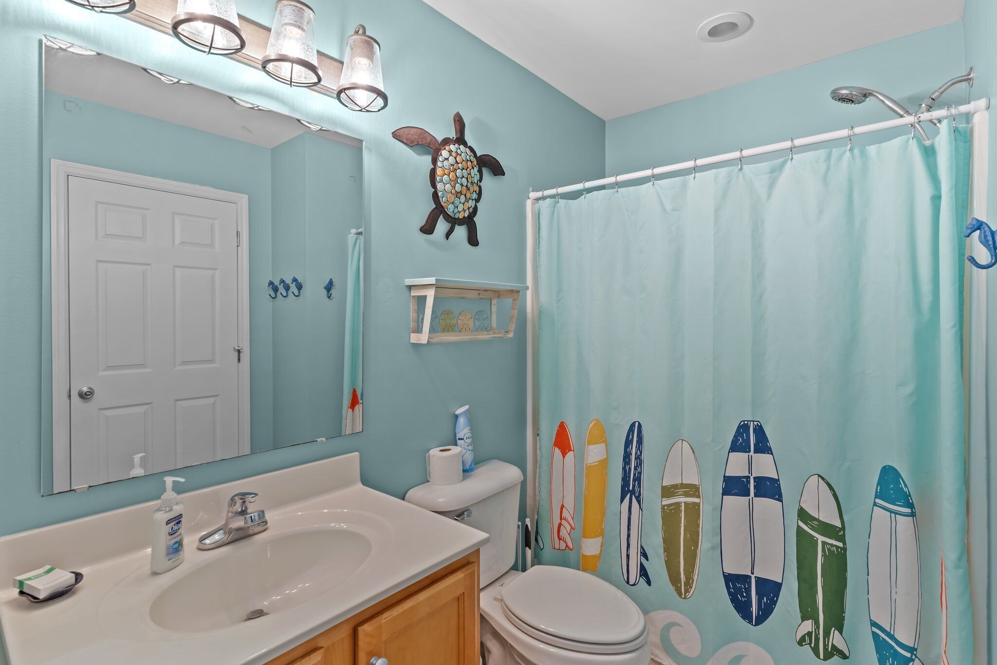 A bathroom with a light blue wall, a white sink, a toilet, and a shower curtain with surfboard designs.