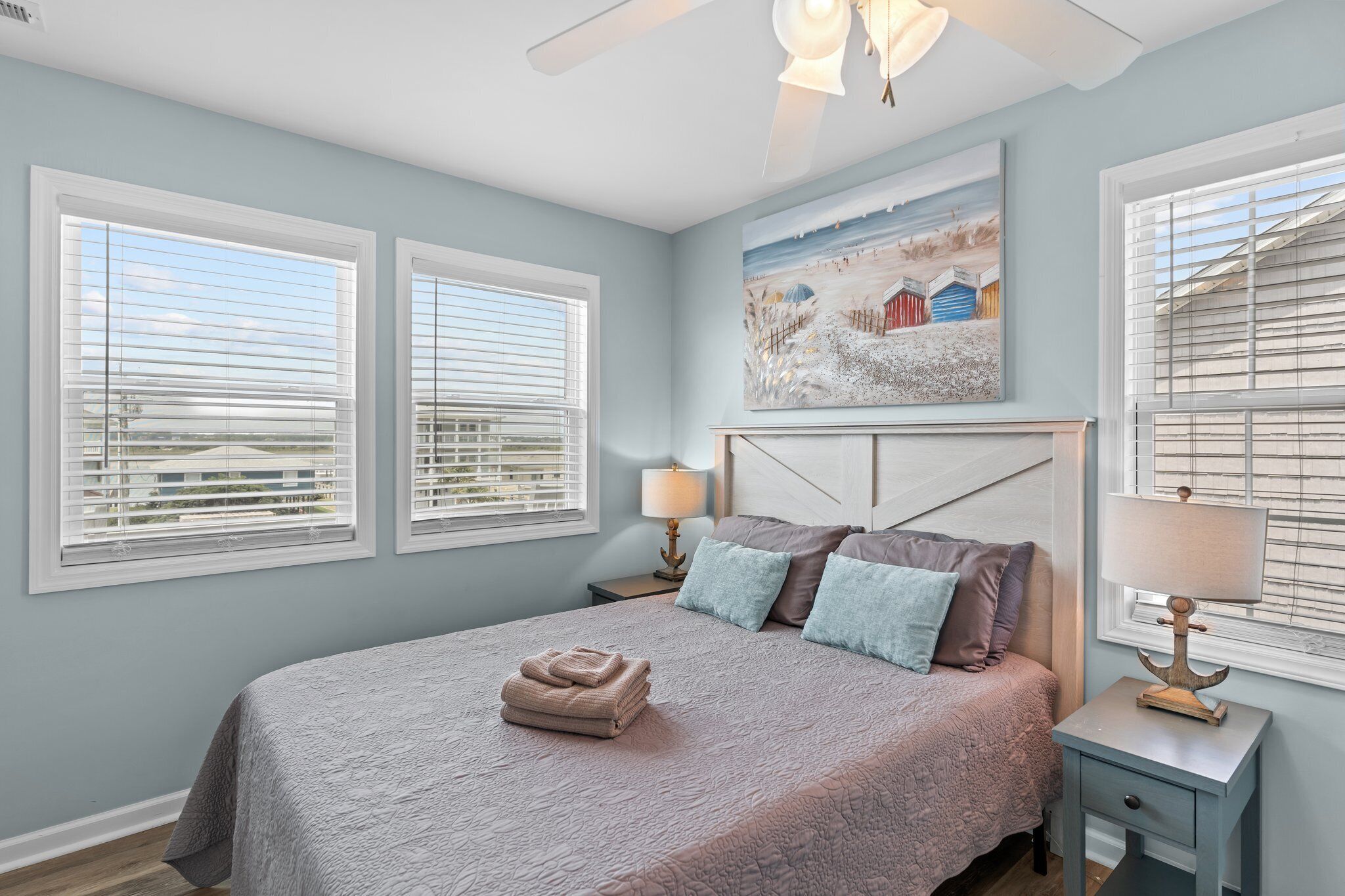 A bedroom with a bed, two bedside tables, a ceiling fan, and a painting on the wall.