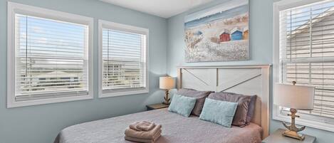 A bedroom with a bed, two bedside tables, a ceiling fan, and a painting on the wall.