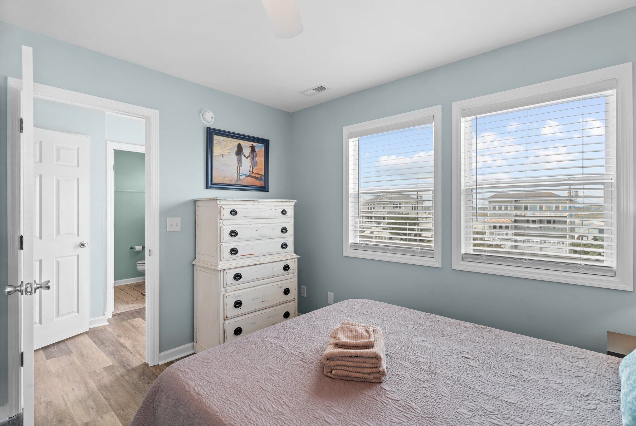 A bedroom with a bed, a dresser, a painting, and a window with blinds.