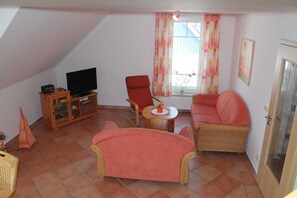 En hyggelig stue med fjernsyn, rød lænestol, sofa og et lille bord med en tepotte.
