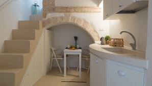 A compact kitchen with a stone archway, a dining area with chairs, and a staircase. - Terrazza Blu Cobalto by Wonderful Italy (Ostuni)