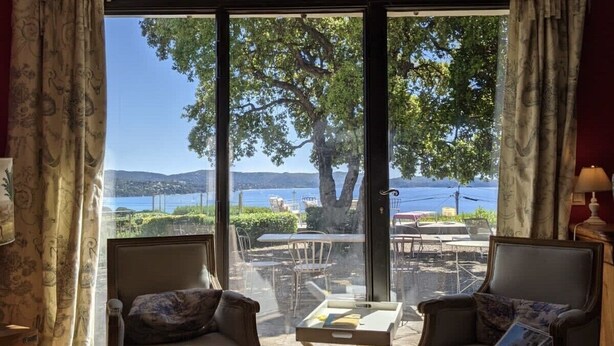 A room with two armchairs facing a large sliding glass door leading to an outdoor dining area with a view of a lake and trees.