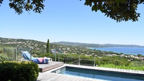 A pool area with a view of a coastal town and hills.