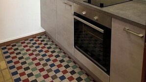 Une cuisine avec des meubles gris, un plan de travail en acier inoxydable, un four encastré et un sol à carreaux aux couleurs vives.