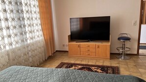 Une pièce avec un lit, un téléviseur posé sur un meuble en bois, un tabouret de bar et un tapis à motifs.