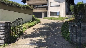 Un bâtiment moderne à deux étages, doté d’une entrée pavée, d’un mur de pierre sur la gauche et d’un portail en métal sur la droite.