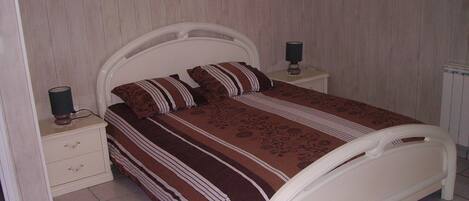 A bedroom with a bed, two bedside tables, and a wall-mounted lamp.