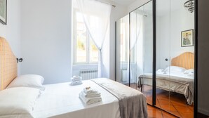 A hotel room with two beds, a large window with sheer curtains, a mirror, and a tiled floor.