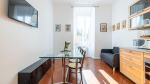 A modern kitchen with a glass dining table, wooden cabinets, and a grey sofa.