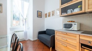 A compact kitchen with a microwave, a small sofa, and a cabinet with a fruit bowl.