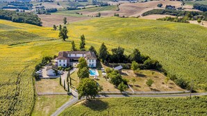 Una casa grande con piscina, rodeada de campos y árboles.