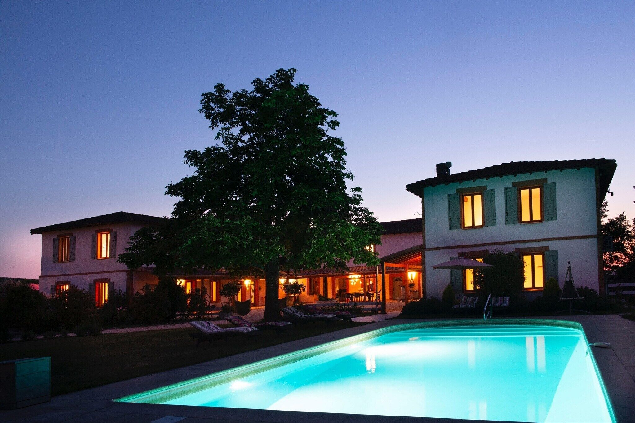 A two-story building with a swimming pool, outdoor seating, and a tree.