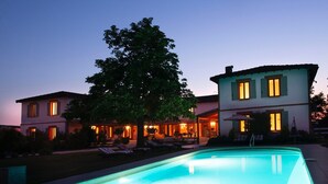 Un edificio de dos pisos con piscina, asientos al aire libre y un árbol.