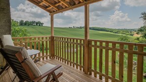 Una terraza de madera con mesa y sillas, con vistas a un campo verde y árboles.
