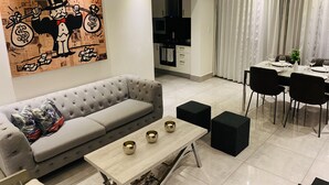 Una sala de estar moderna con un sofá gris, una mesa de centro de madera y una zona de comedor con una mesa blanca para cuatro personas.
