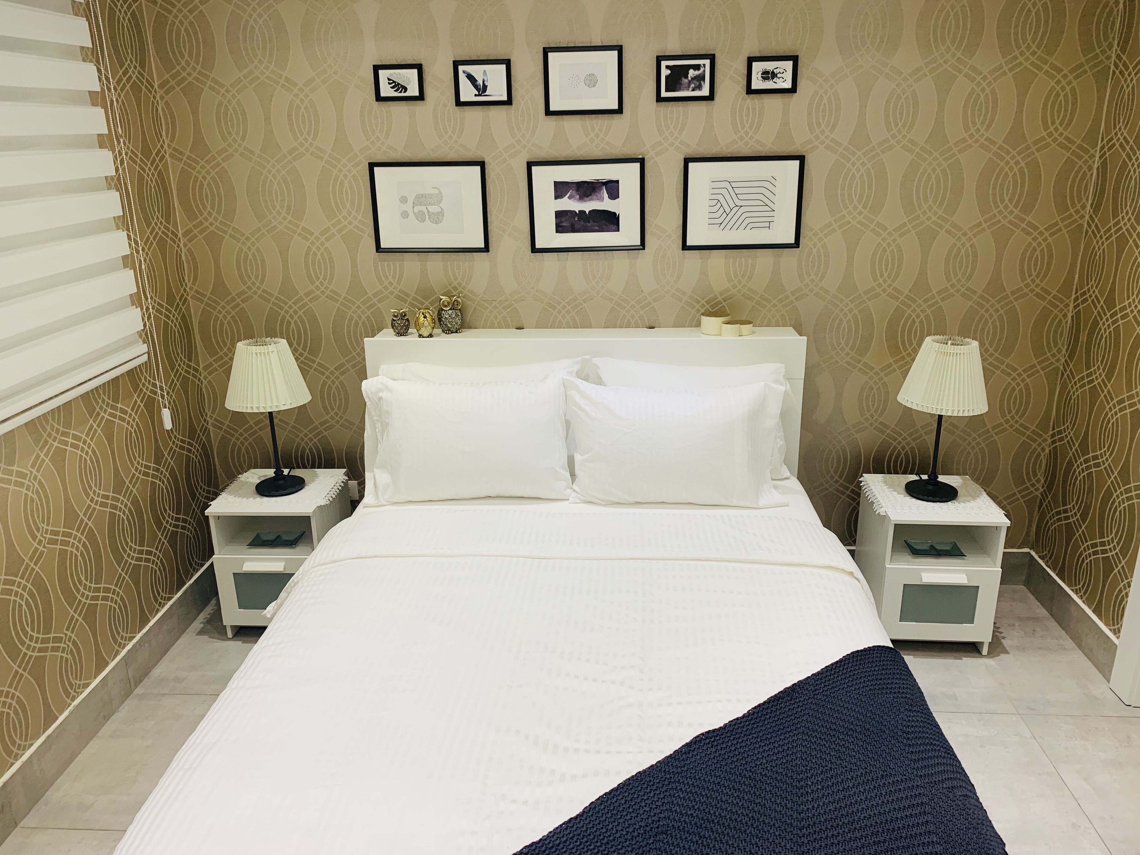 A neatly arranged bedroom with a bed, two bedside tables, lamps, and a wall with framed artwork.