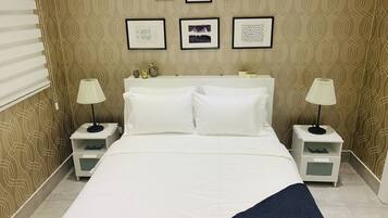 A neatly arranged bedroom with a bed, two bedside tables, lamps, and a wall with framed artwork.
