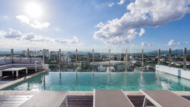 Piscina infinita en la azotea con sillones y vista panorámica de la ciudad.