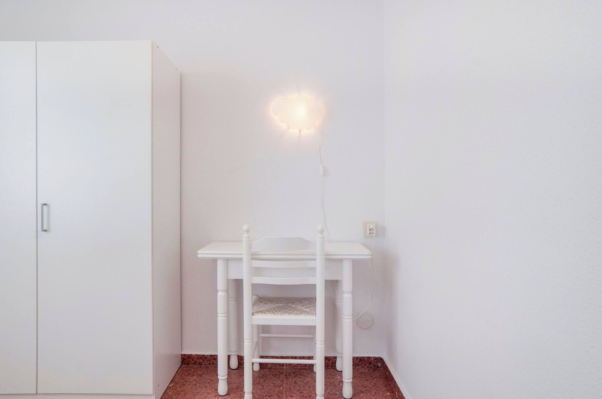 A white desk with a lamp in a room with a white wardrobe and a tiled floor.
