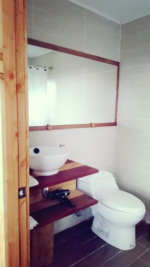 Een compacte badkamer met een wit toilet, een witte wastafel en een houten opbergmeubel.