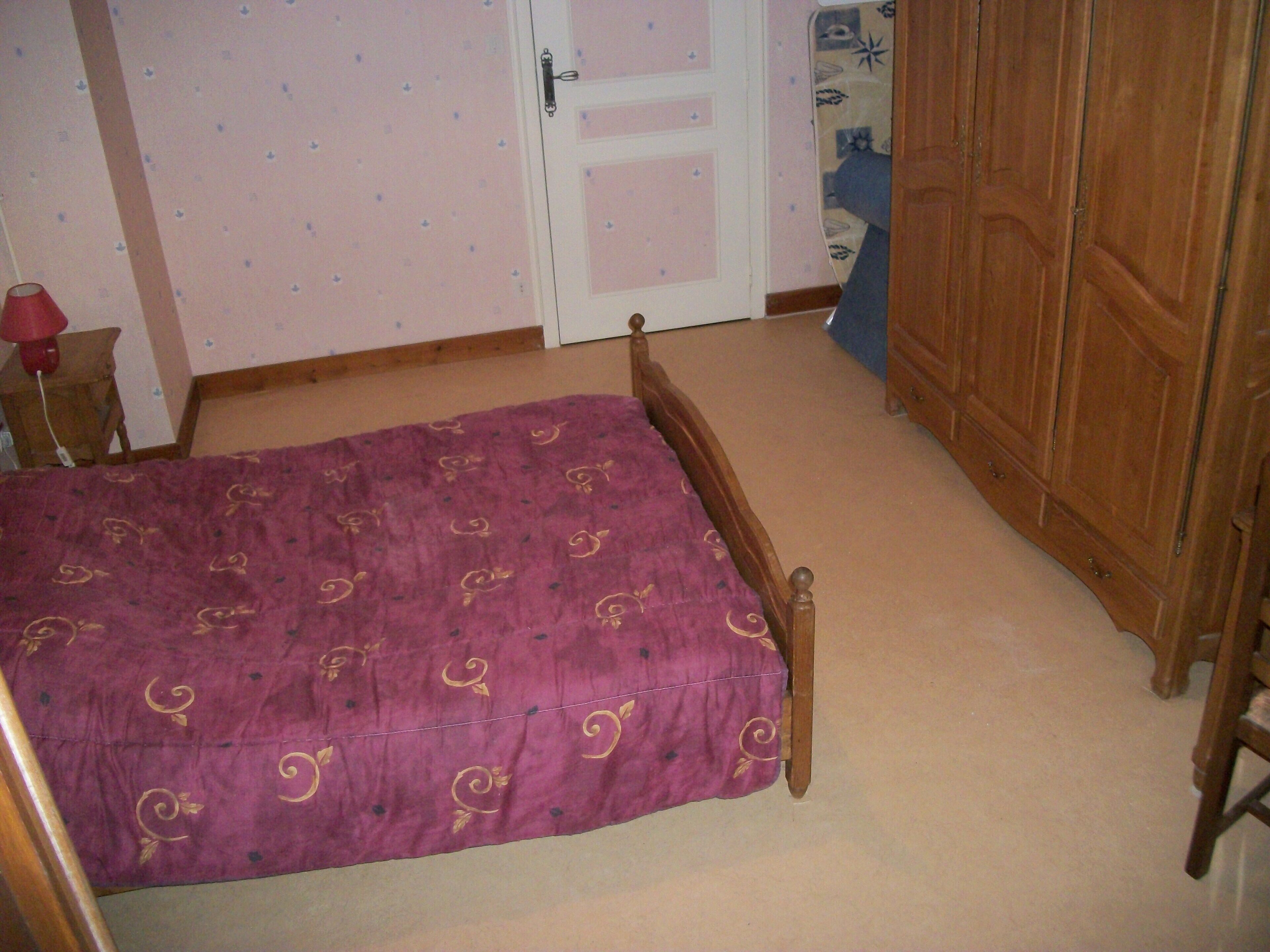 A bedroom with a wooden bed, a wardrobe, and a door with a patterned curtain.