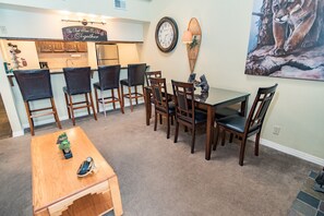Un comedor con una mesa y sillas de madera, una cocina al fondo y un cuadro de león en la pared.