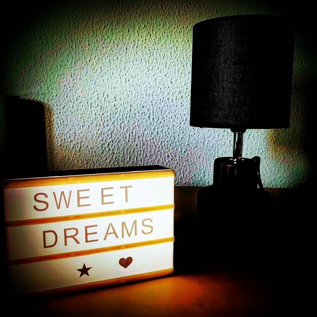 A bedside table with a lamp and a sign that reads "SWEET DREAMS".