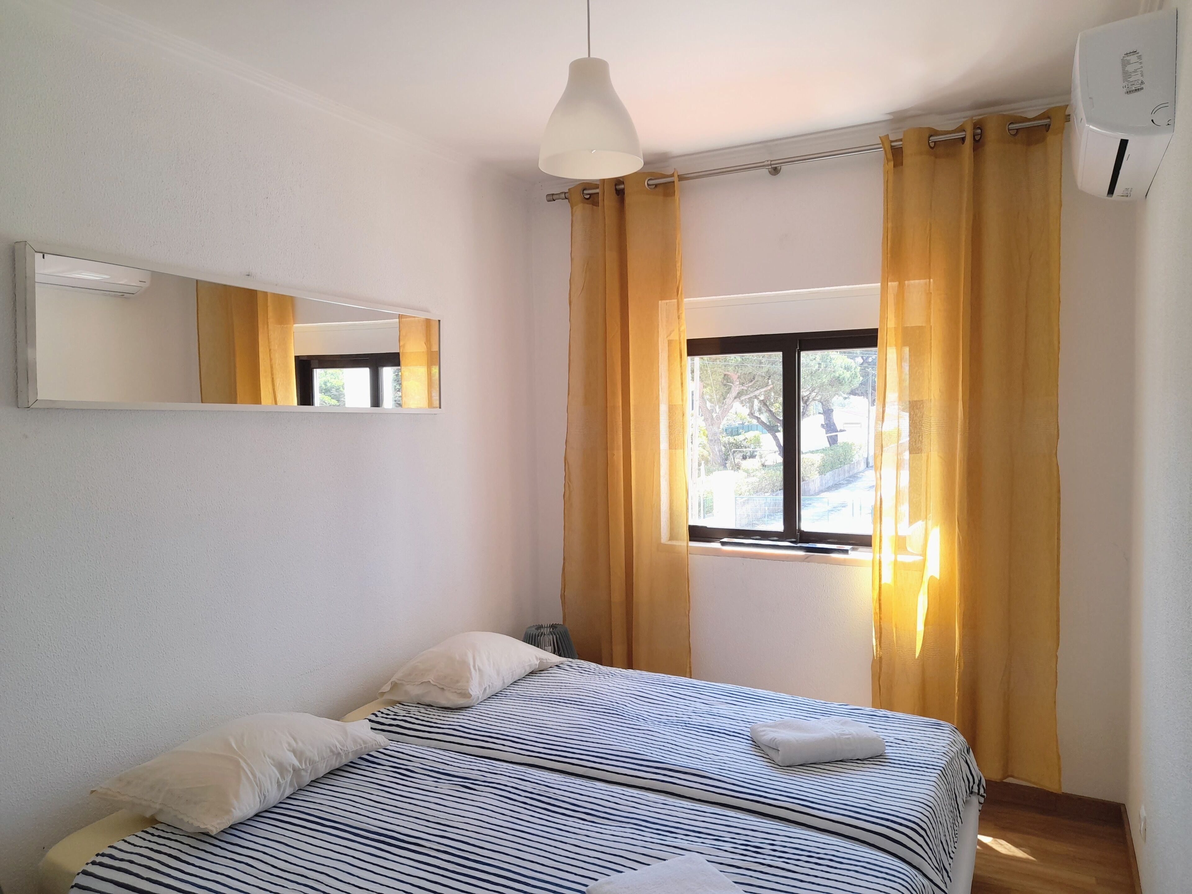 Un dormitorio con cama, ventana con cortinas, luz de techo y equipo de aire acondicionado.