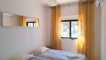 Un dormitorio con cama, ventana con cortinas, luz de techo y equipo de aire acondicionado.