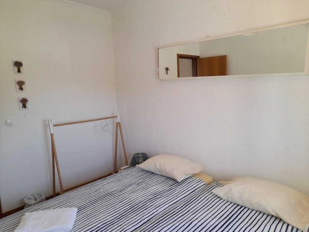 A small, sparsely furnished room with a bed, a mirror, and a wooden drying rack.