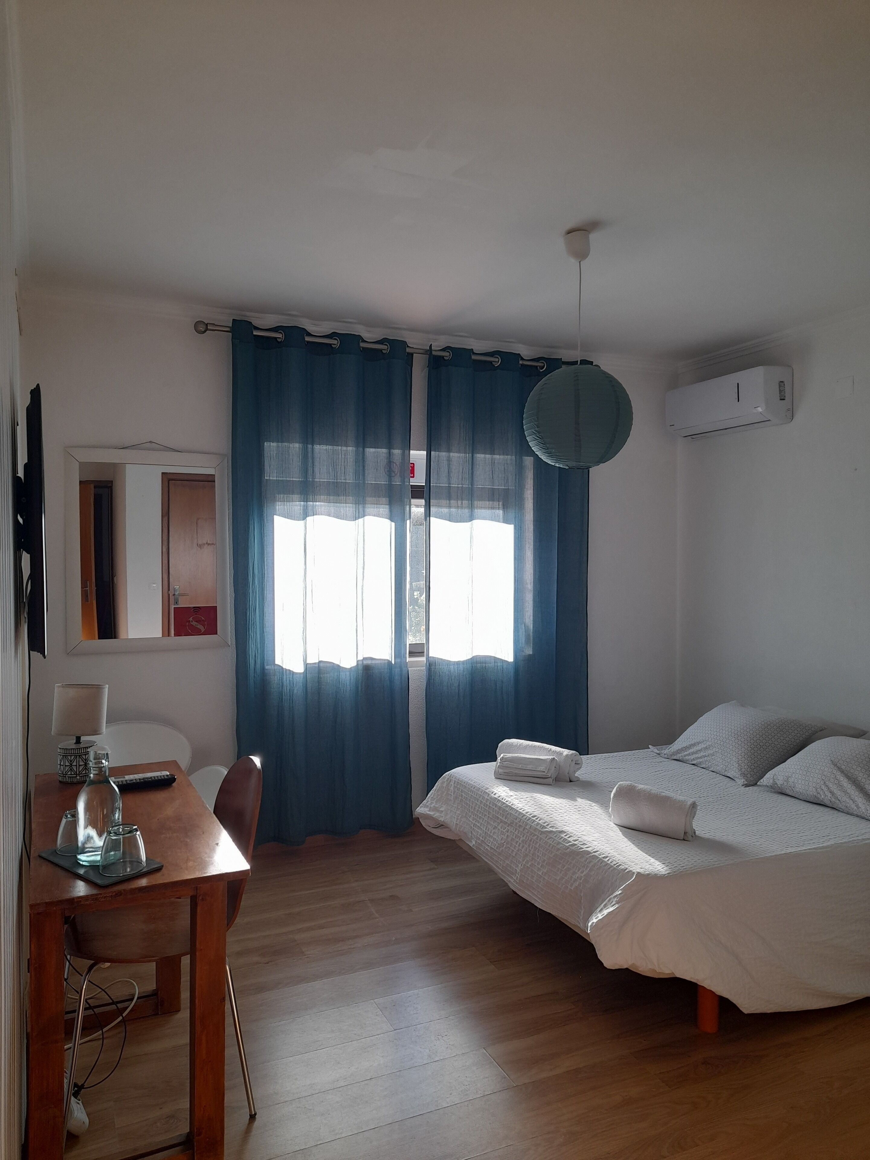 Ein Schlafzimmer mit einem Bett, einem Schreibtisch mit Lampe und einem fenster mit Vorhängen.