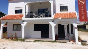 A two-story building with a red-tiled roof, a balcony with chairs, and a red banner with text. - Sublime Sun & Van, By Meco Stays (Sesimbra)