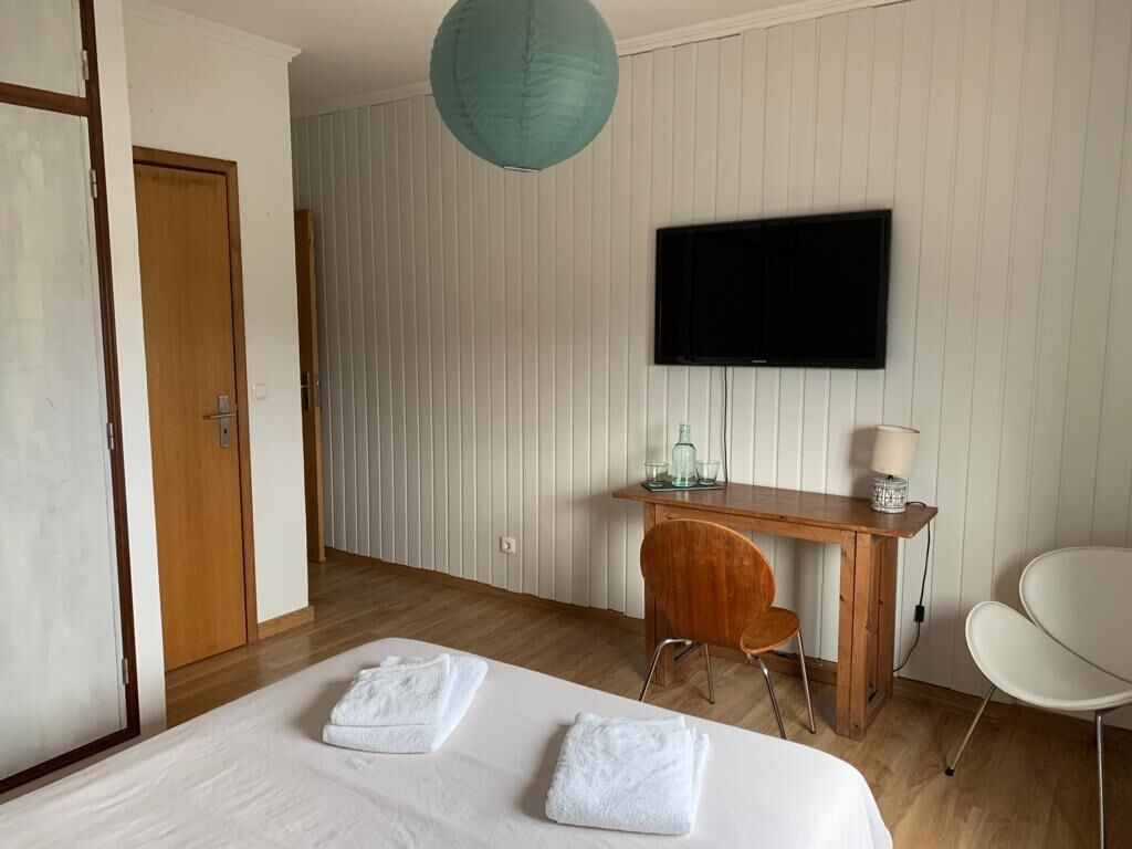 A hotel room with a bed, a desk, a chair, a television, and a hanging light fixture.
