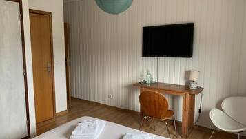 A hotel room with a bed, a desk, a chair, a television, and a hanging light fixture.