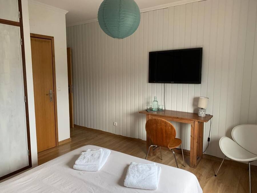 A hotel room with a bed, a desk, a chair, a television, and a hanging light fixture.