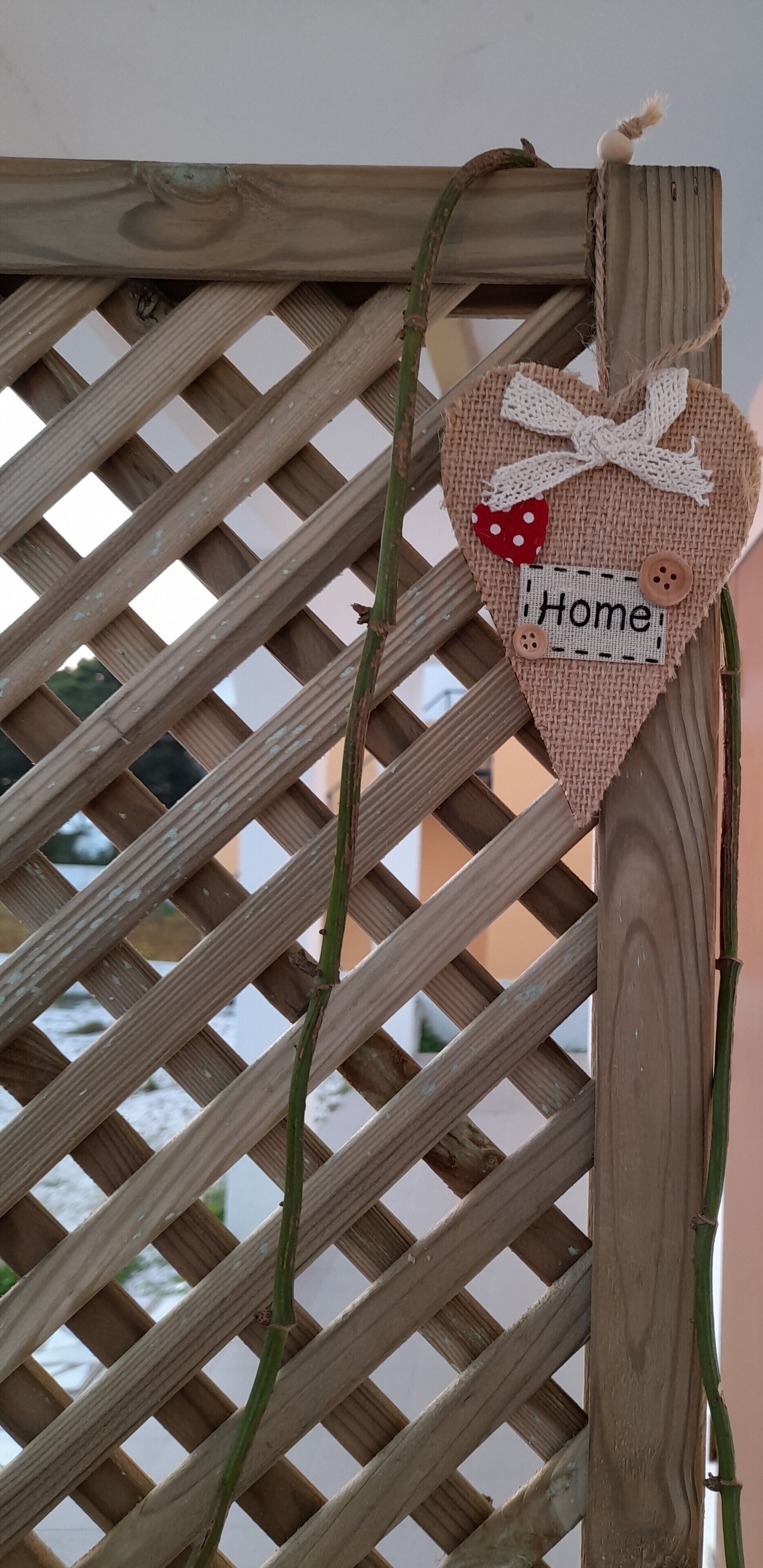 Een hartvormige decoratie met de tekst ‘Home’ aan een houten lattenstructuur.