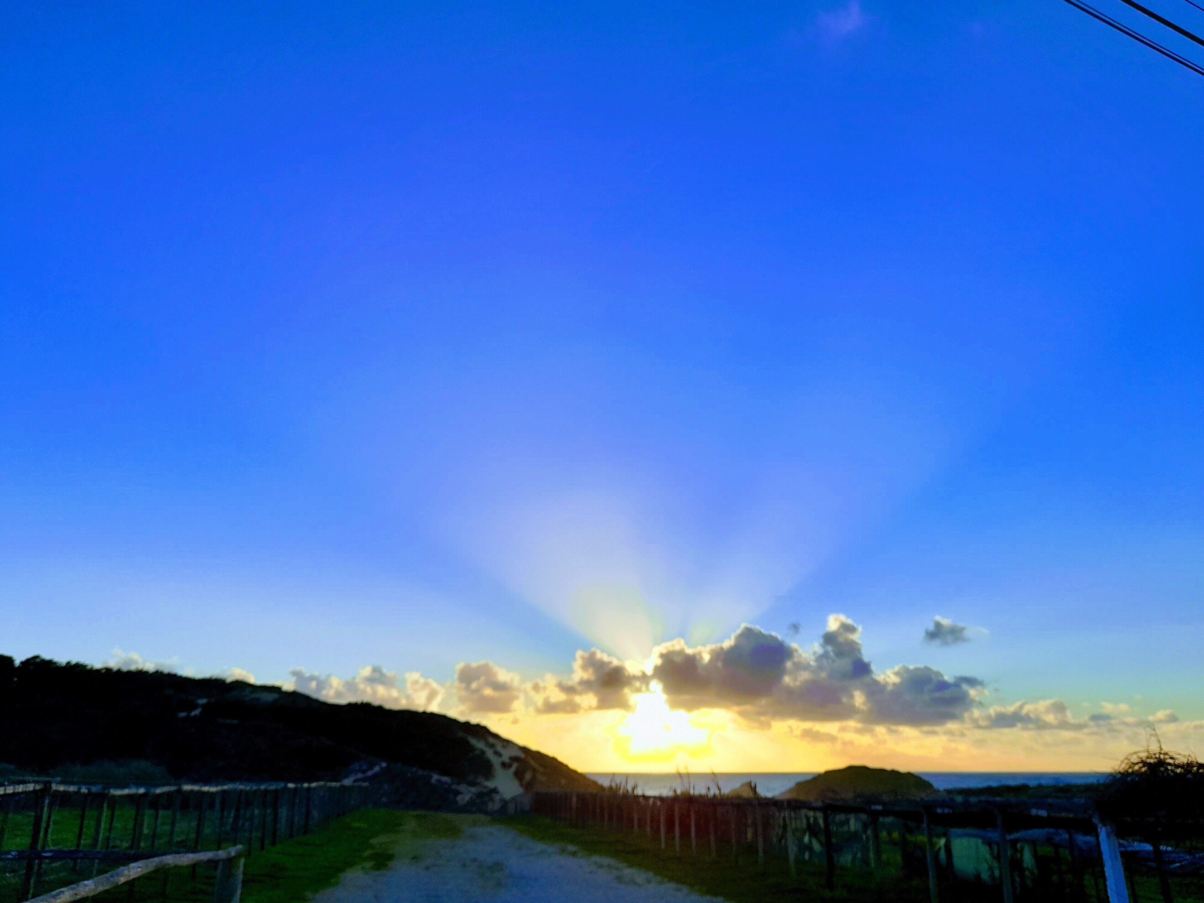 Un atardecer sobre un paisaje costero con un sendero de tierra que lleva a una cerca.