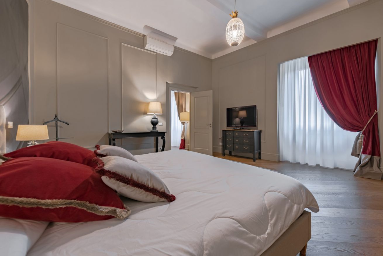 A bedroom with a large bed, a television, a desk, and a wardrobe.